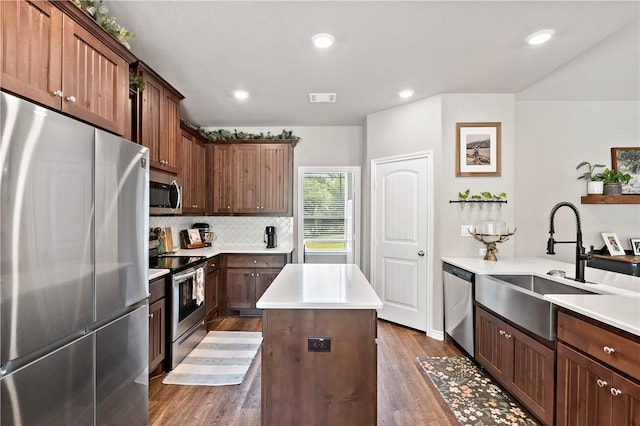 kitchen featuring appliances with stainless steel finishes, a kitchen island, dark wood-style flooring, a sink, and visible vents
