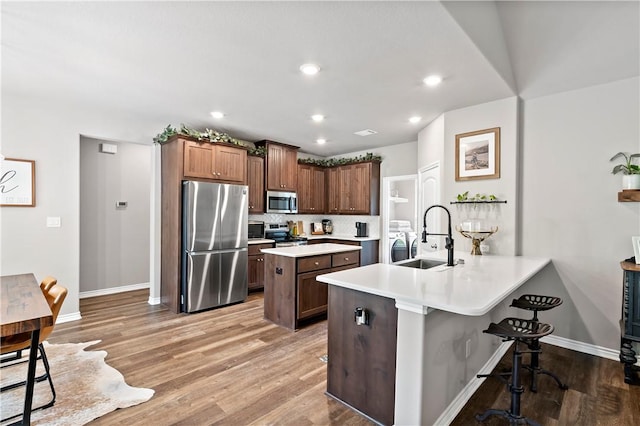 kitchen featuring light wood finished floors, a sink, stainless steel appliances, a kitchen bar, and a peninsula