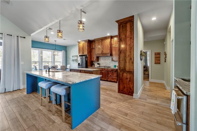 kitchen with a breakfast bar, decorative light fixtures, backsplash, stainless steel fridge with ice dispenser, and a center island with sink