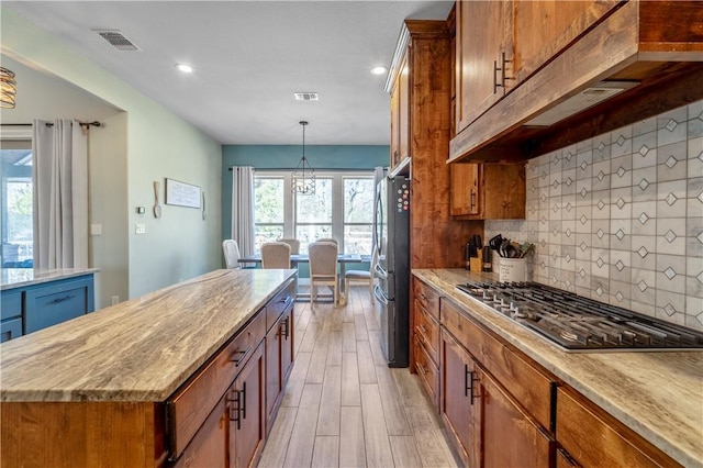 kitchen with a kitchen island, appliances with stainless steel finishes, tasteful backsplash, hanging light fixtures, and light hardwood / wood-style floors