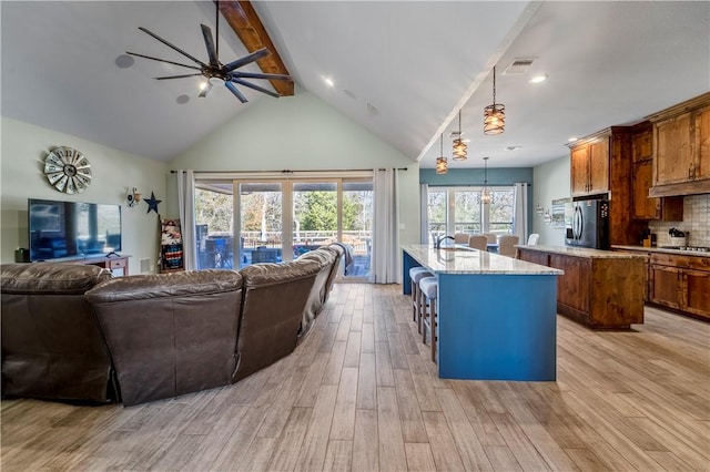 kitchen featuring light hardwood / wood-style flooring, hanging light fixtures, beam ceiling, a kitchen island with sink, and backsplash