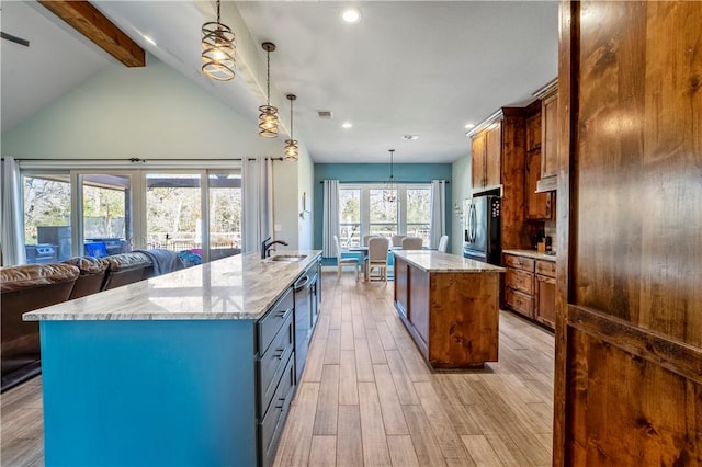 kitchen with a spacious island, sink, light stone counters, decorative light fixtures, and appliances with stainless steel finishes