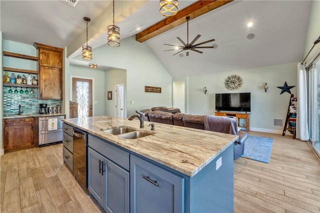 kitchen with decorative light fixtures, sink, decorative backsplash, a kitchen island with sink, and light stone counters