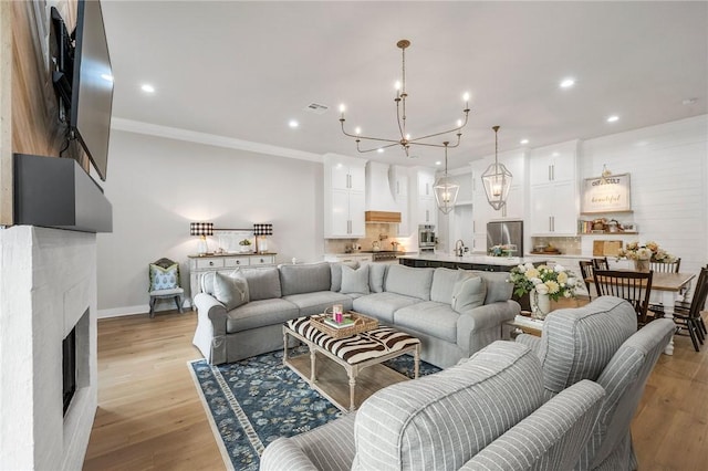 living area with light wood-type flooring, recessed lighting, a chandelier, a fireplace, and ornamental molding
