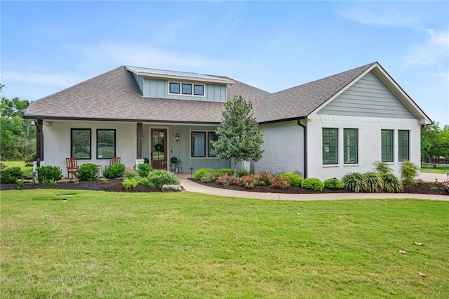 view of front of house with brick siding, a porch, a front yard, and a shingled roof