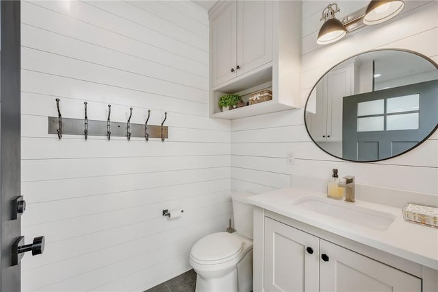 half bathroom with wooden walls, vanity, and toilet