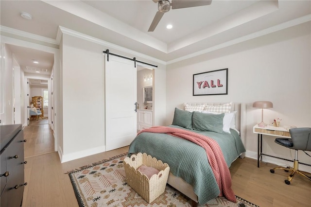 bedroom with a barn door, light wood-style floors, baseboards, and ornamental molding