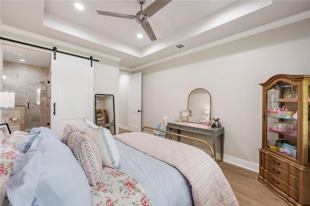 bedroom featuring a barn door, light wood-type flooring, visible vents, recessed lighting, and a raised ceiling