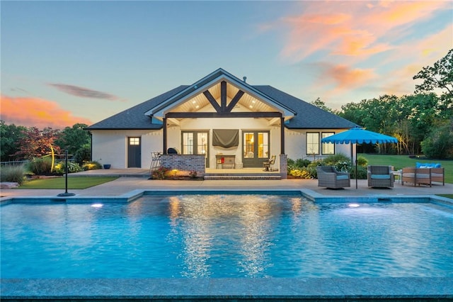 back of house at dusk featuring outdoor lounge area, french doors, a patio, and an outdoor pool