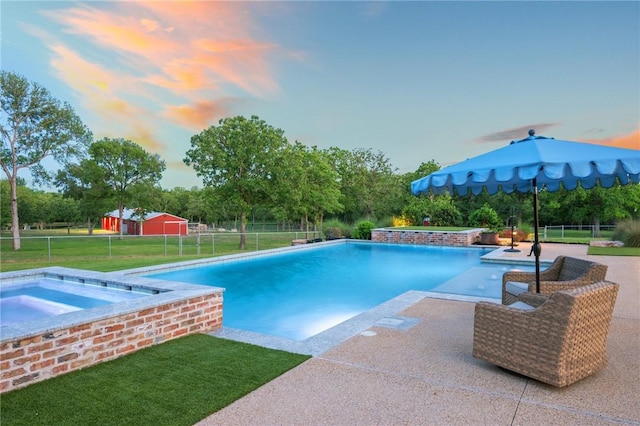pool at dusk featuring an in ground hot tub, fence, a patio, a yard, and an outdoor pool