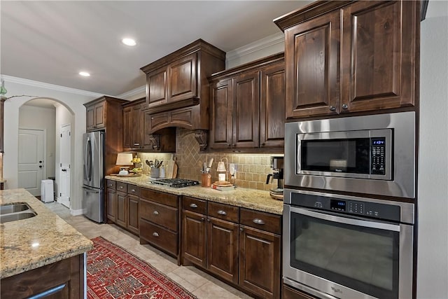 kitchen featuring light stone counters, arched walkways, stainless steel appliances, backsplash, and ornamental molding