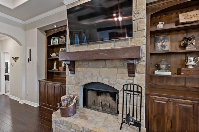 living room with arched walkways, a stone fireplace, dark wood-type flooring, baseboards, and crown molding