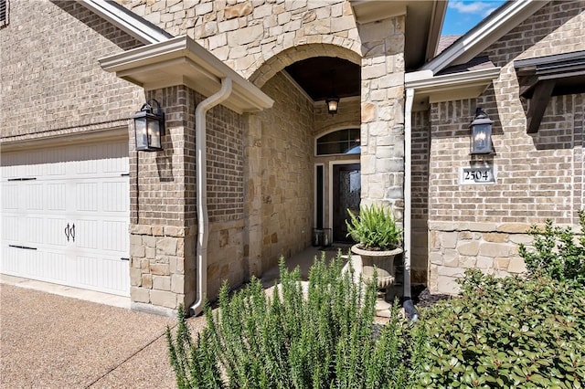 doorway to property with a garage, stone siding, and brick siding