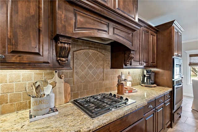 kitchen featuring dark brown cabinetry, decorative backsplash, appliances with stainless steel finishes, light stone counters, and crown molding