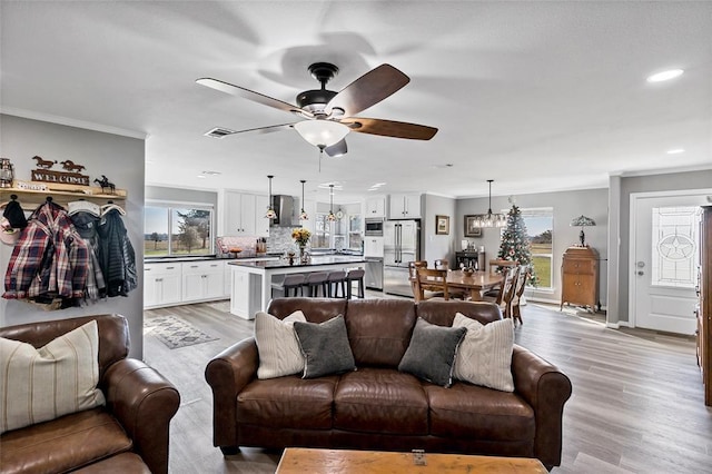 living room featuring ceiling fan with notable chandelier, ornamental molding, and light hardwood / wood-style flooring