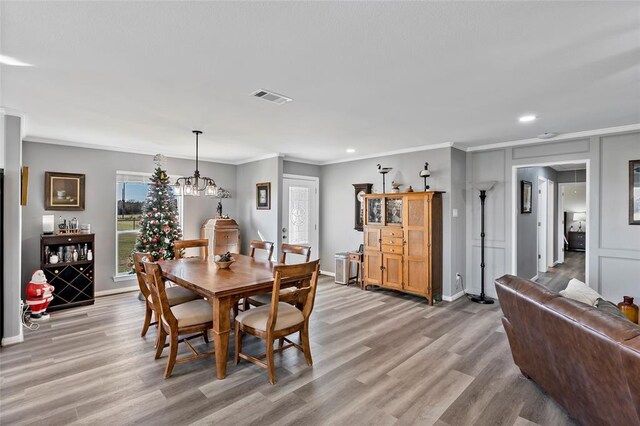 dining area with light hardwood / wood-style flooring, crown molding, and a notable chandelier