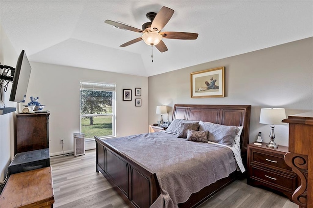 bedroom with light hardwood / wood-style floors, vaulted ceiling, and ceiling fan