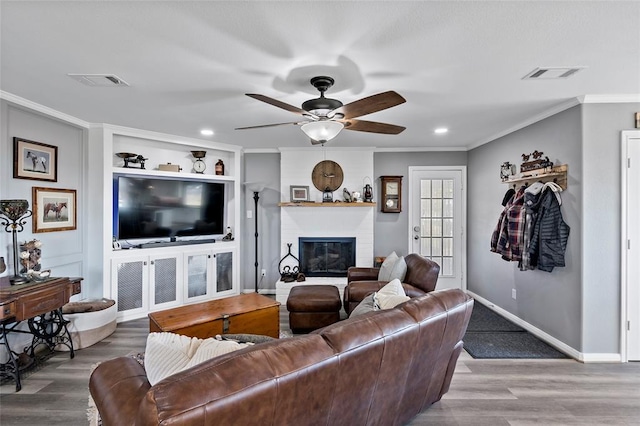 living room with a brick fireplace, crown molding, ceiling fan, and hardwood / wood-style flooring