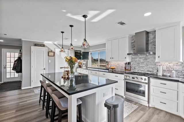 kitchen featuring white cabinets, wall chimney range hood, hanging light fixtures, high end stainless steel range, and a kitchen bar