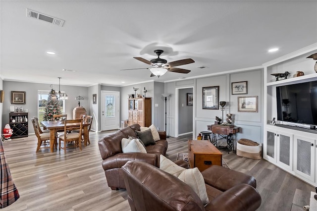 living room with ceiling fan with notable chandelier, light wood-type flooring, and crown molding