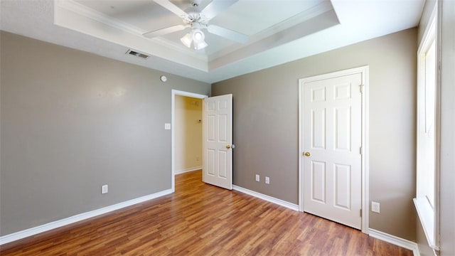 unfurnished bedroom with hardwood / wood-style flooring, ceiling fan, crown molding, and a raised ceiling