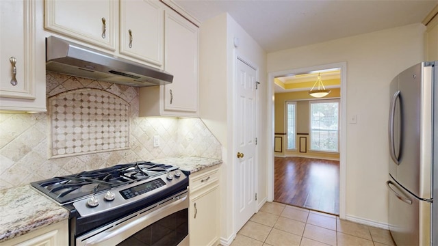 kitchen with light tile patterned floors, appliances with stainless steel finishes, light stone counters, decorative backsplash, and a raised ceiling