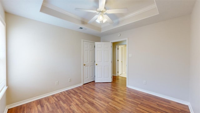 unfurnished bedroom featuring a tray ceiling, dark wood-type flooring, ornamental molding, and ceiling fan