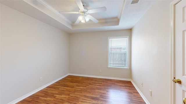 empty room featuring dark hardwood / wood-style floors, ceiling fan, ornamental molding, and a tray ceiling