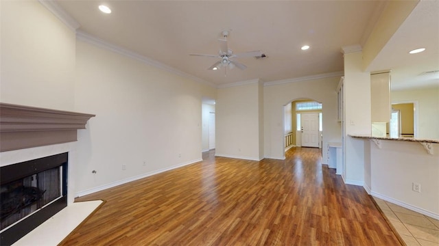 unfurnished living room featuring ceiling fan, ornamental molding, and wood-type flooring