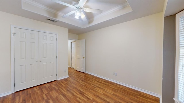 unfurnished bedroom featuring crown molding, hardwood / wood-style flooring, ceiling fan, a raised ceiling, and a closet