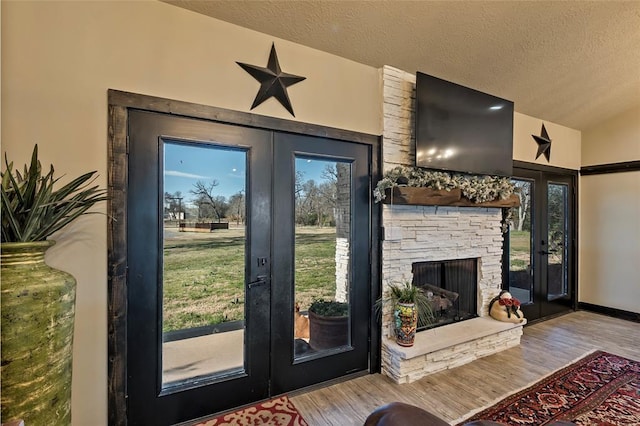 entryway featuring a textured ceiling, wood finished floors, french doors, a fireplace, and lofted ceiling