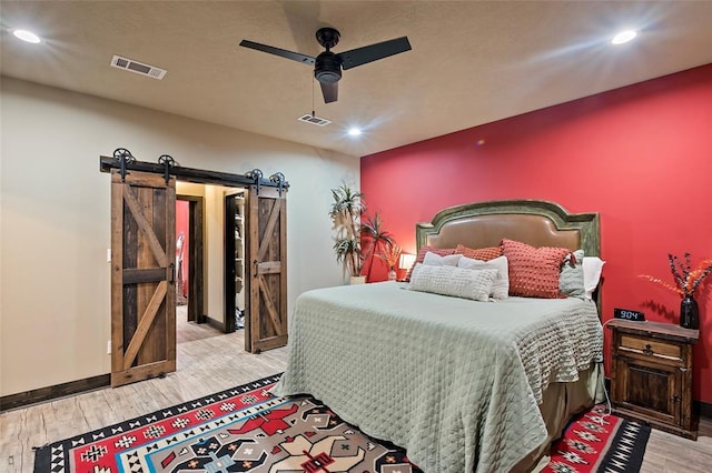 bedroom with a barn door, recessed lighting, visible vents, and light wood finished floors