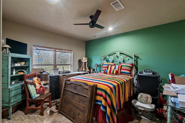 bedroom with visible vents, a textured ceiling, a ceiling fan, and wood finished floors