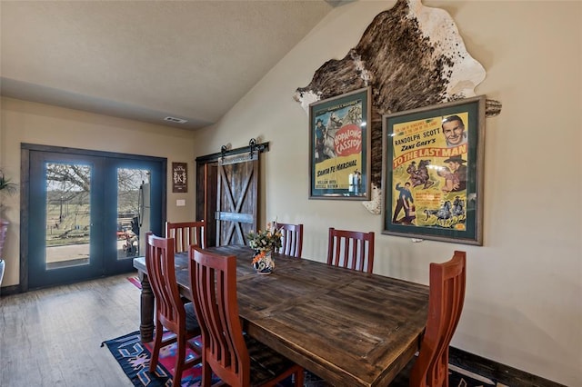 dining space with hardwood / wood-style floors, baseboards, visible vents, lofted ceiling, and a barn door