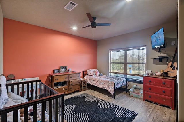 bedroom with wood finished floors, visible vents, and ceiling fan