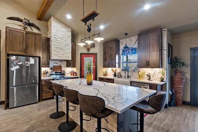 kitchen featuring a kitchen island, a breakfast bar, a sink, stainless steel appliances, and light wood-type flooring