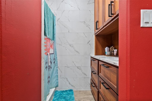 bathroom featuring tiled shower, wood finished floors, vanity, and a textured wall