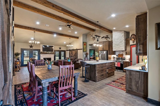 dining space featuring light wood-type flooring, beam ceiling, a fireplace, an inviting chandelier, and high vaulted ceiling