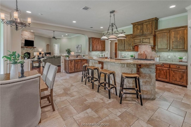 kitchen with a stone fireplace, pendant lighting, a breakfast bar area, a kitchen island, and ceiling fan with notable chandelier