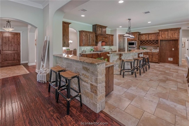 kitchen featuring hanging light fixtures, light stone counters, kitchen peninsula, decorative backsplash, and a breakfast bar