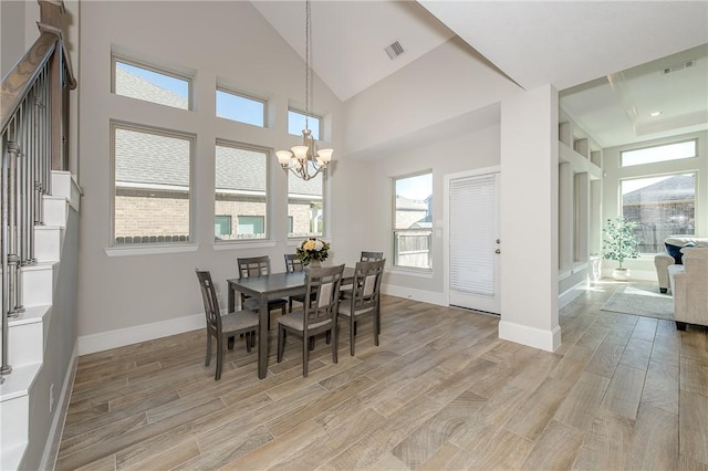 dining room with light hardwood / wood-style floors, high vaulted ceiling, and a notable chandelier