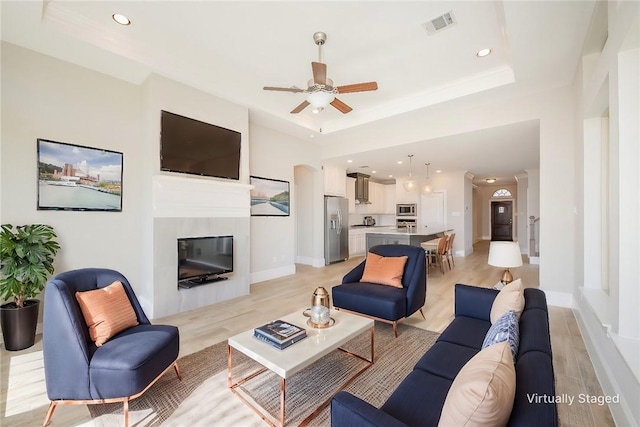 living room featuring a tray ceiling, ceiling fan, and light hardwood / wood-style floors