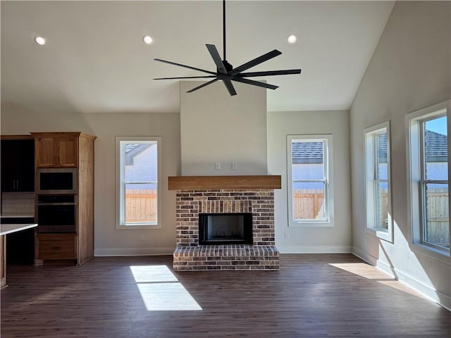 unfurnished living room with ceiling fan, lofted ceiling, dark wood-type flooring, and a brick fireplace