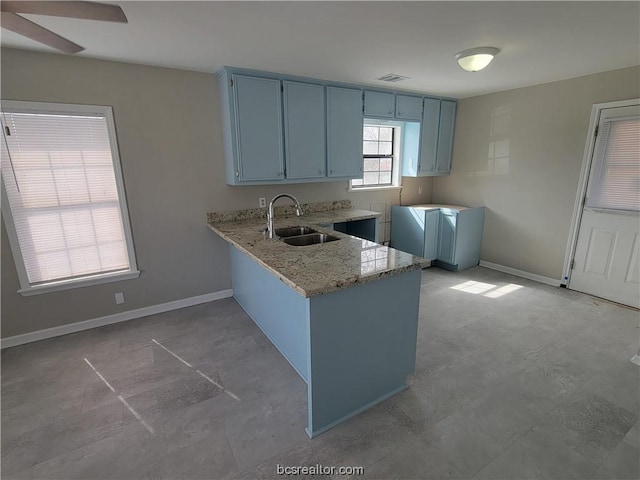 kitchen with kitchen peninsula, light stone counters, ceiling fan, sink, and blue cabinetry