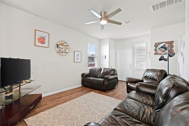 living area featuring baseboards, visible vents, wood finished floors, and a ceiling fan