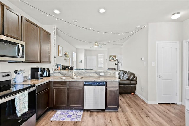 kitchen featuring a sink, appliances with stainless steel finishes, light wood-style floors, open floor plan, and a peninsula