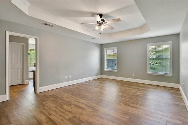 empty room featuring a raised ceiling, crown molding, a ceiling fan, wood finished floors, and plenty of natural light