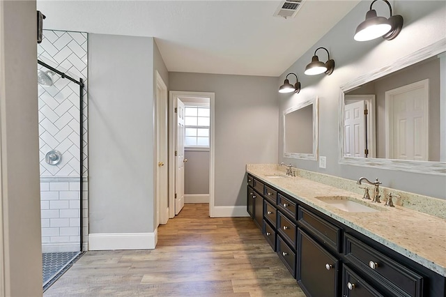 full bathroom featuring tiled shower, double vanity, wood finished floors, and baseboards