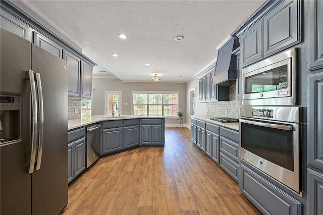 kitchen featuring stainless steel appliances, a peninsula, a sink, gray cabinetry, and ornamental molding