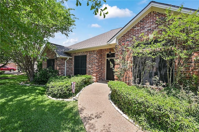 ranch-style home featuring brick siding, a front yard, and roof with shingles